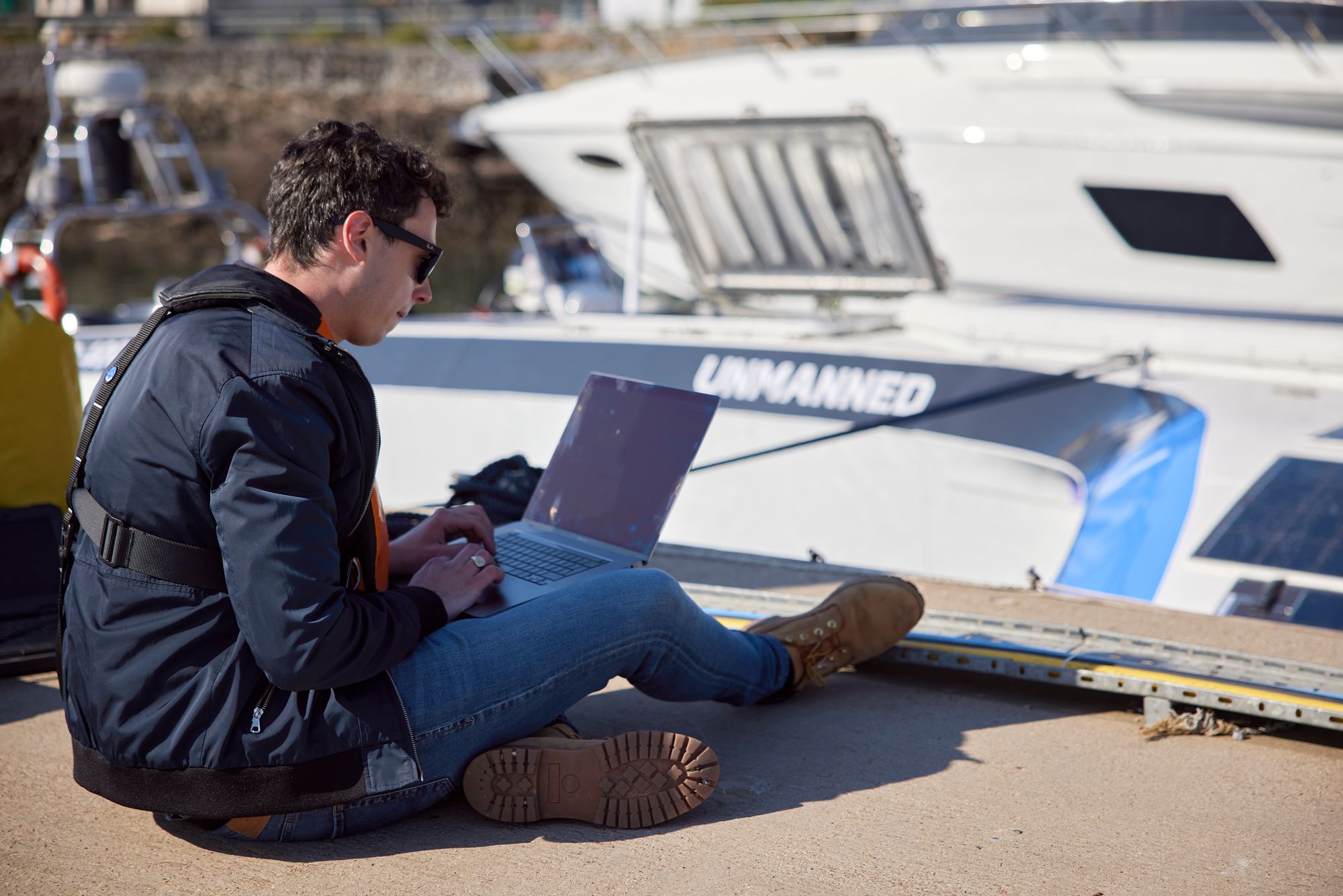 A photo of me sitting on the dock by the Mayflower Autonomous Ship with my laptop.